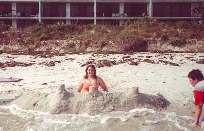 Courtney poses in her sandcastle as her serf, Aaron looks on